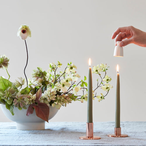 White flower shaped ceramic candle snuffer about to extinguish the flame on a taper candle